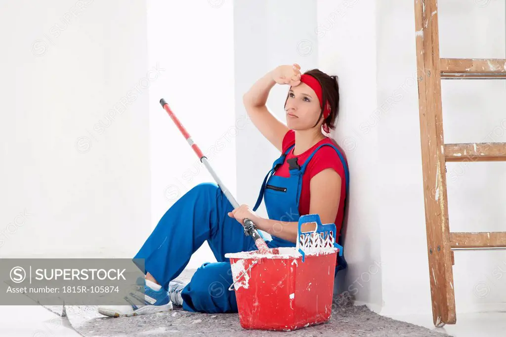 Germany, Bavaria, Young woman tired, sitting with paint tin and brush