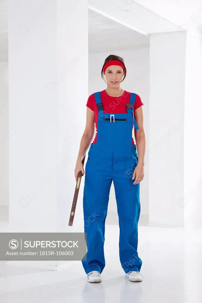 Germany, Bavaria, Young woman with overall, holding spirit level, portrait