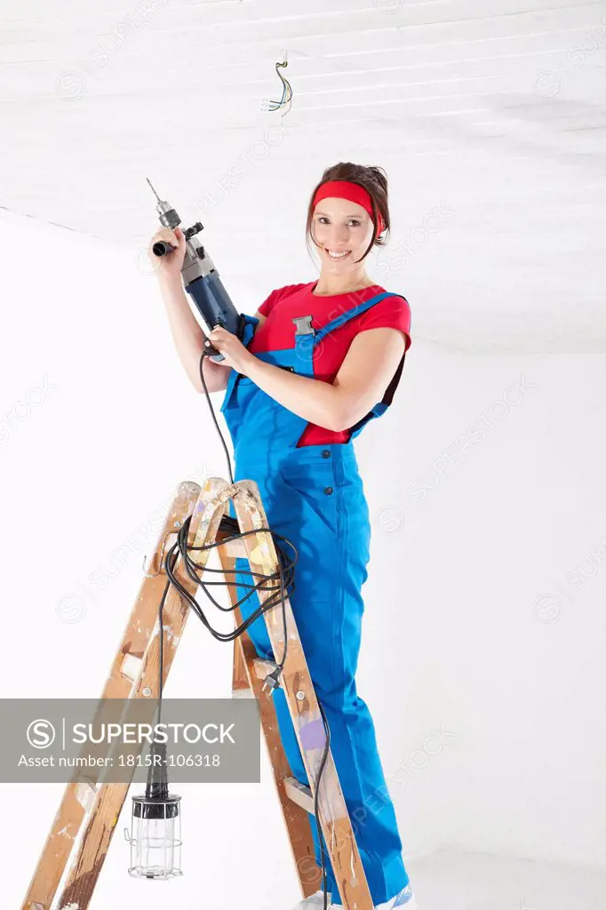 Germany, Bavaria, Young woman drilling with electric drill
