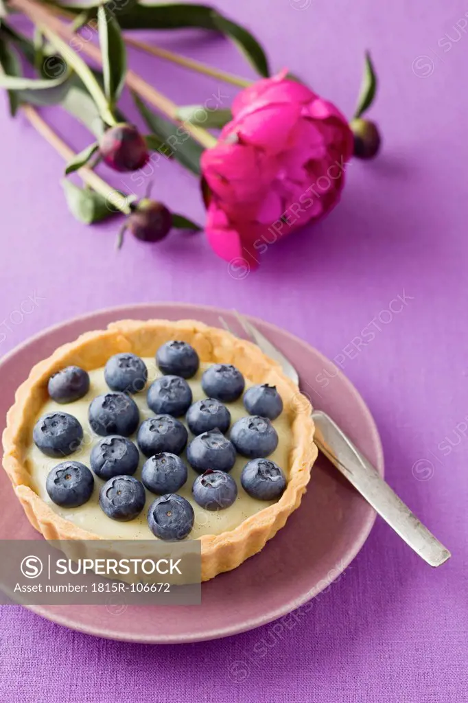 Blueberry tart with vanilla pudding with peony on table