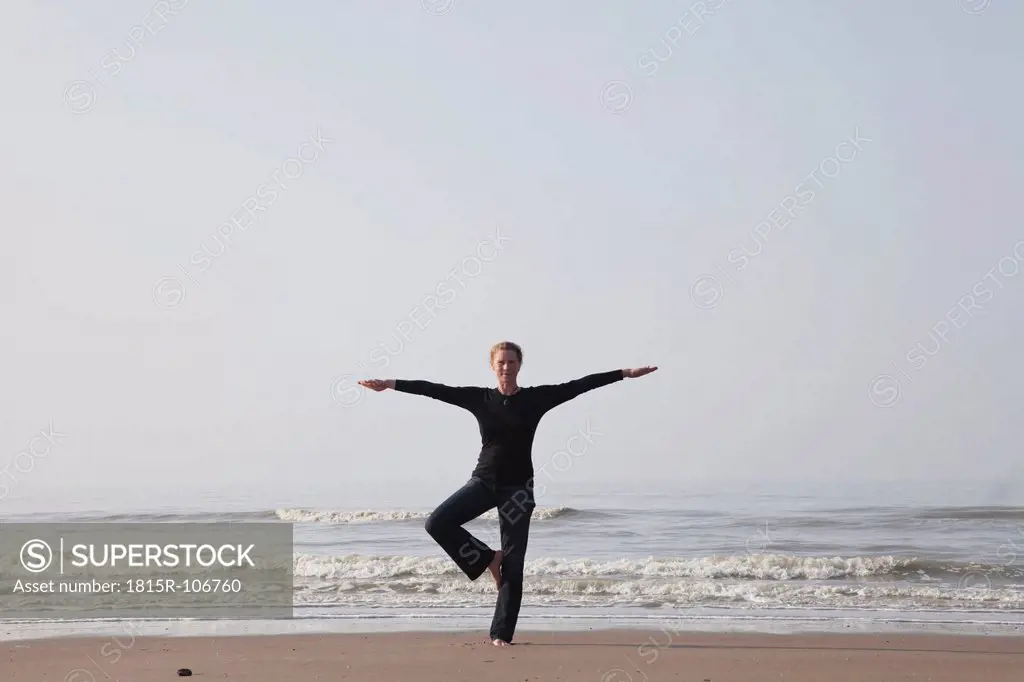 Belgium, Young woman standing in tree pose at North Sea