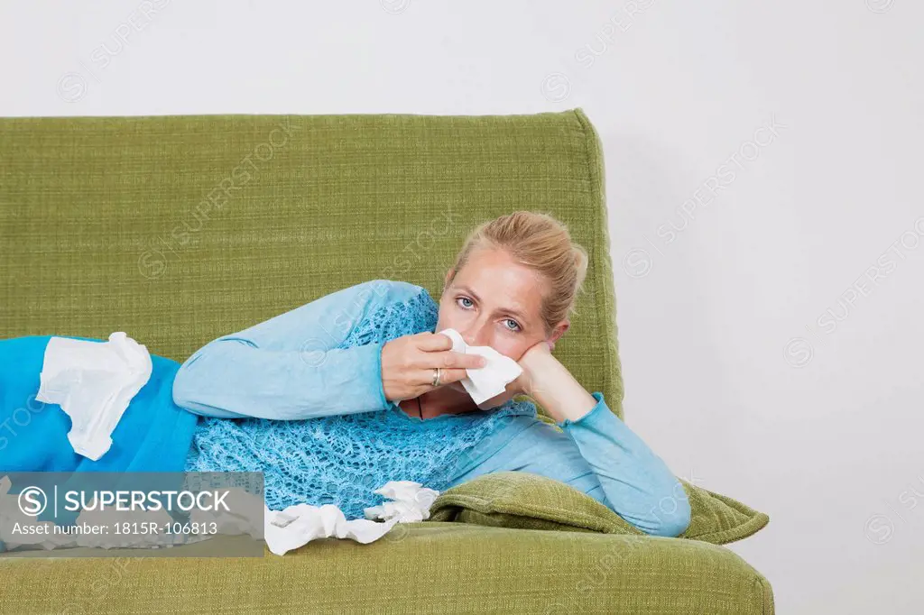 Germany, Cologne, Mature woman blowing nose while lying on sofa