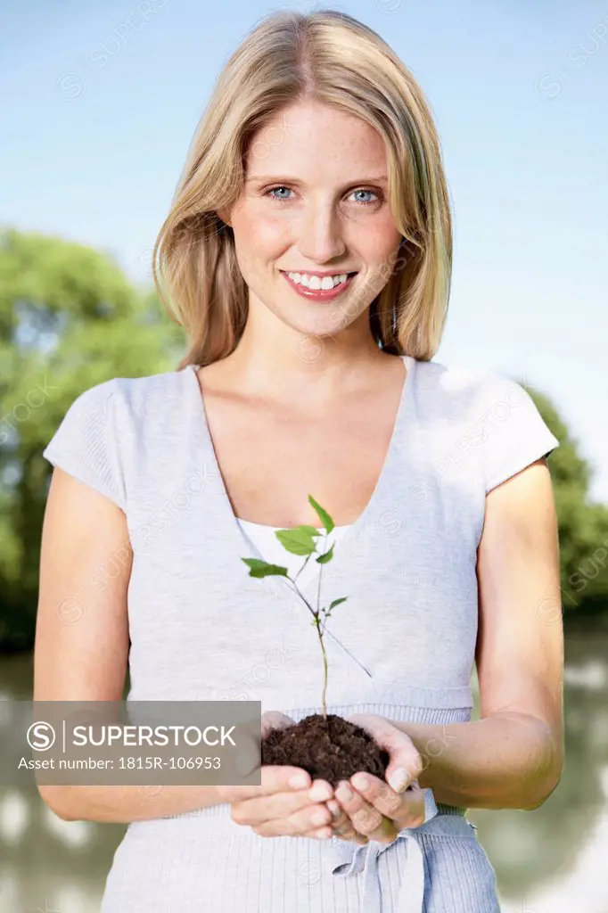 Germany, Cologne, Young woman holding seedling, smiling, portrait