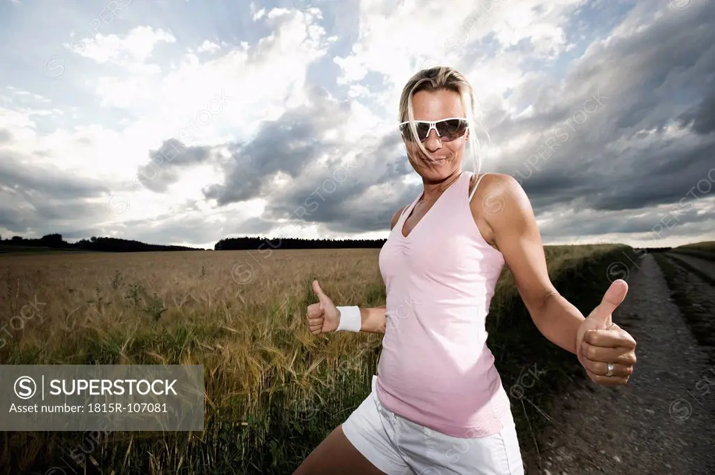 Germany, Bavaria, Mature woman showing thumbs up in grain field