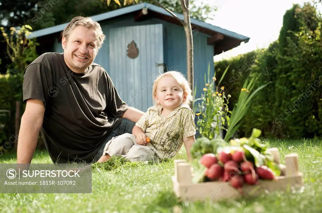 Germany, Bavaria, Father and son sitting in garden, smiling, portrait