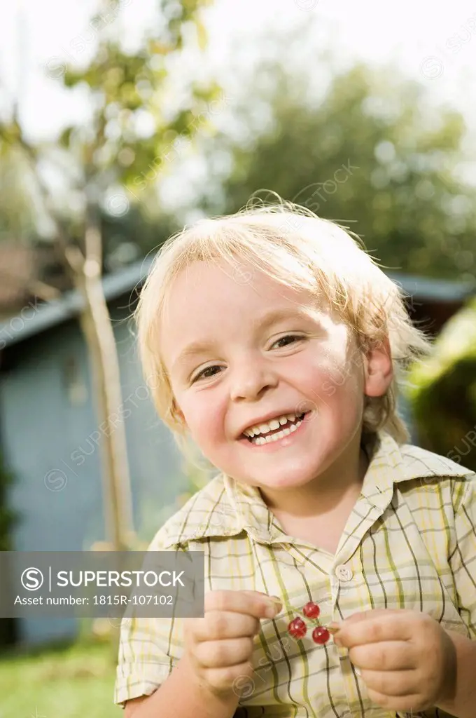 Germany, Bavaria, Boy holding red currants, smiling, portrait