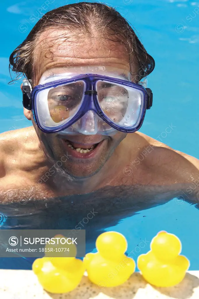 Man in swimming pool looking at plastic ducks