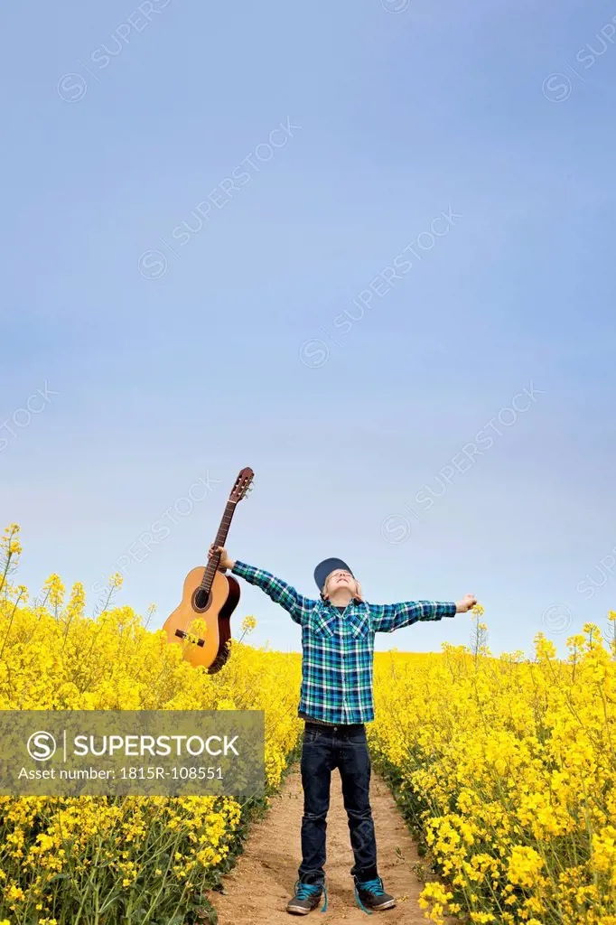 Germany, Hamburg, Boy standing in field with acoustic guitar