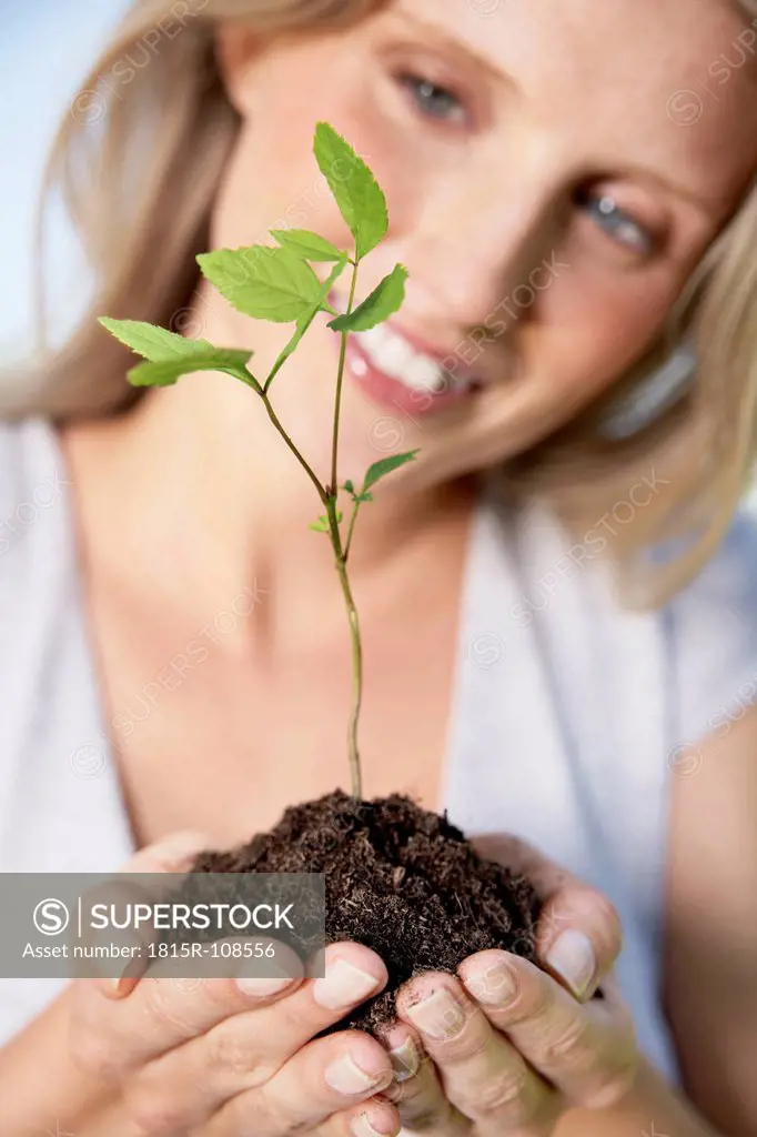 Germany, Cologne, Young woman holding seedling, smiling