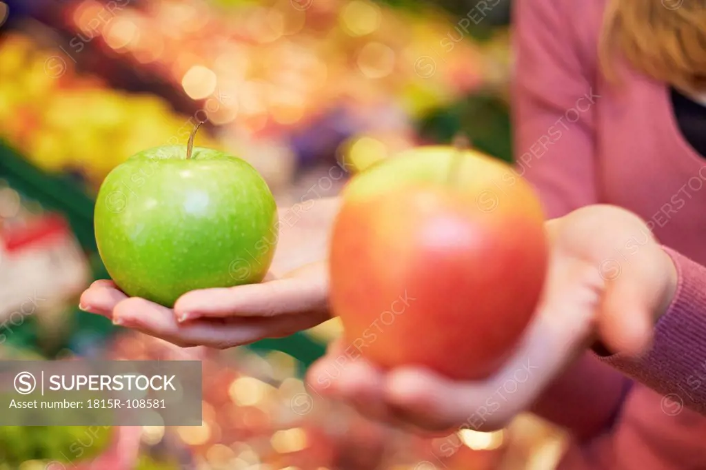 Germany, Cologne, Young woman comparing apples in supermarket