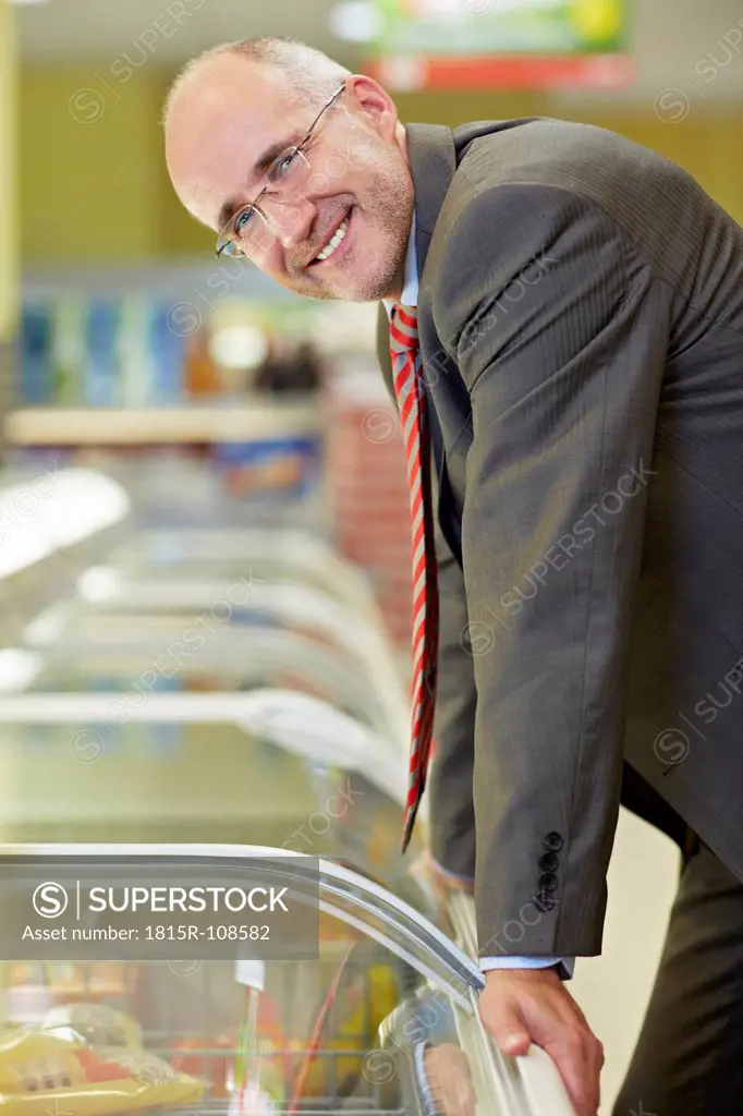 Germany, Cologne, Mature man standing at freezer in supermarket