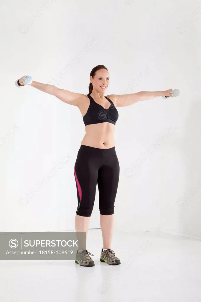Young woman exercising with dumbbell, smiling