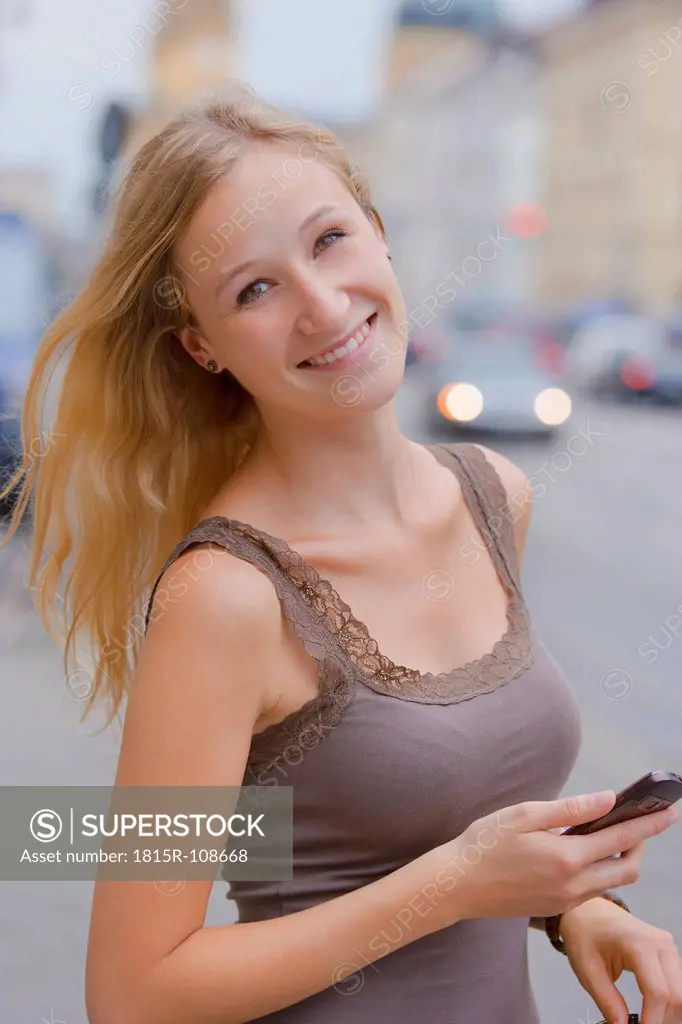 Germany, Bavaria, Munich, Young woman with smart phone in front of Bavarian State Library at Ludwigstrasse