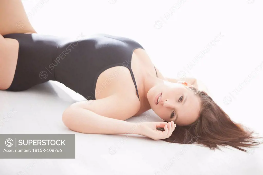 Young woman in black bodysuit, lying on white background