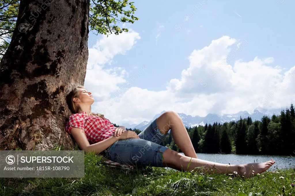 Germany, Bavaria, Young woman lying on grass under tree
