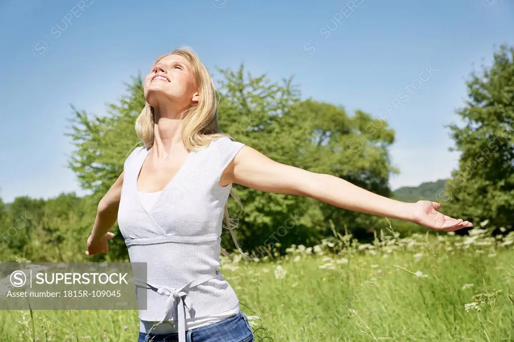 Germany, Cologne, Young woman stretching in meadow