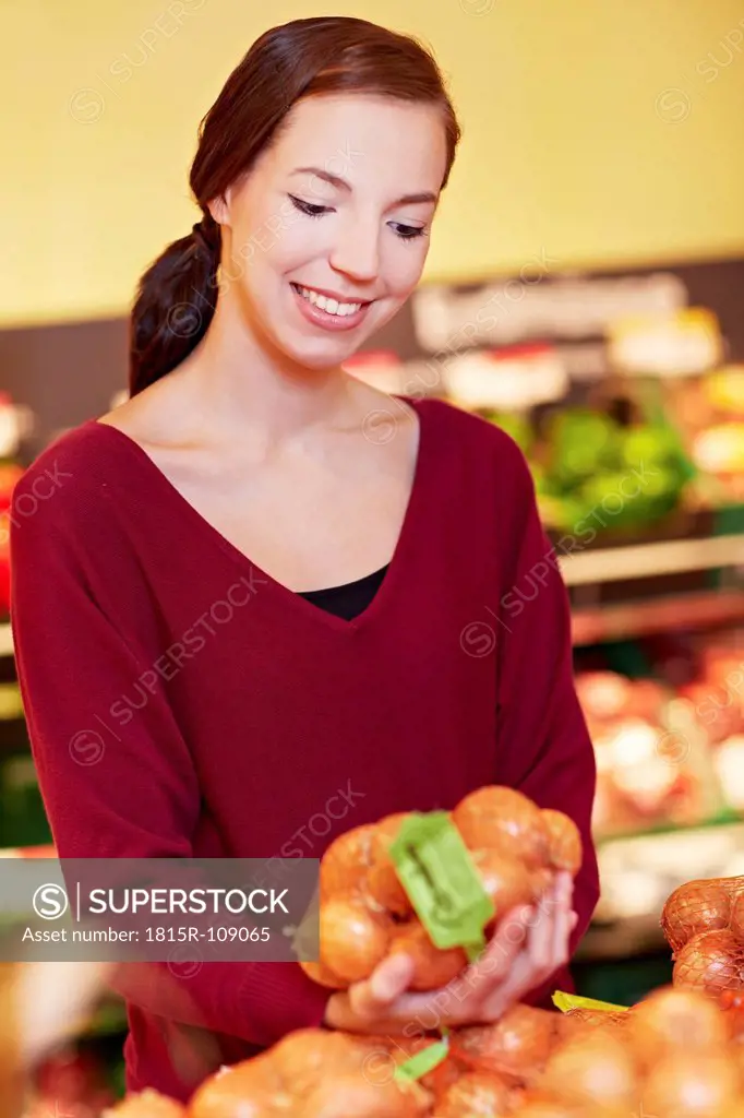 Germany, Cologne, Young woman with onions in supermarket