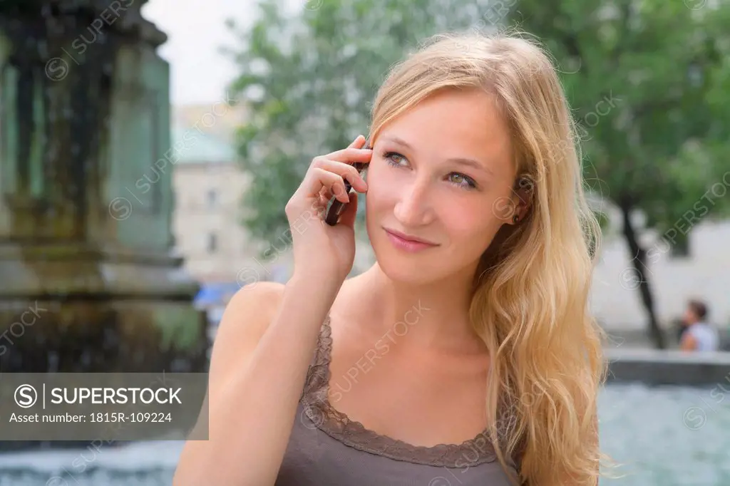 Germany, Bavaria, Munich, Young woman talking on phone in front of Ludwig Maximilian University