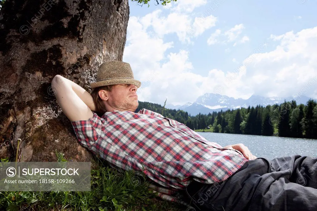 Germany, Bavaria, Mid adult man lying on grass under tree