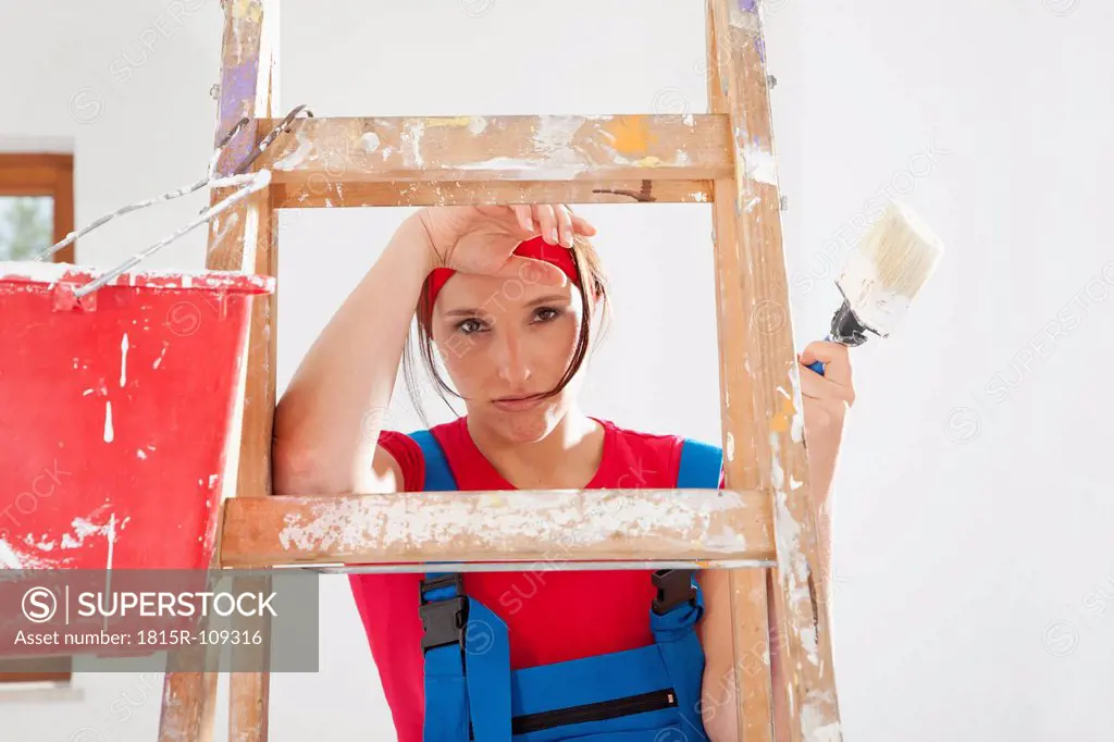 Germany, Bavaria, Young woman standing on step ladder with paint brush