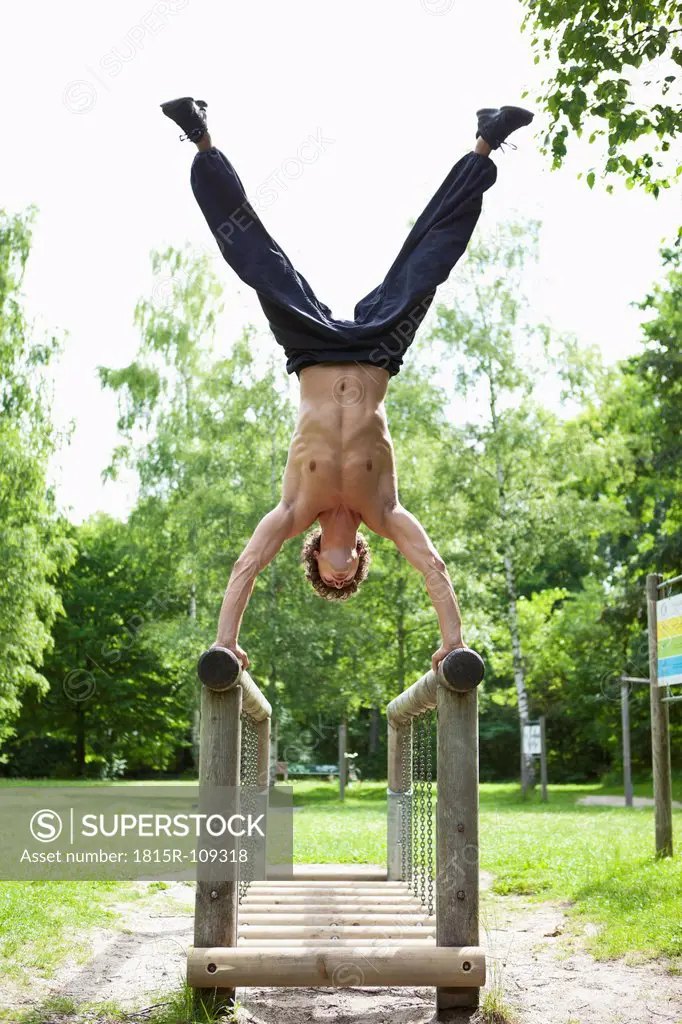 Germany, Bavaria, Young man doing handstand on railing