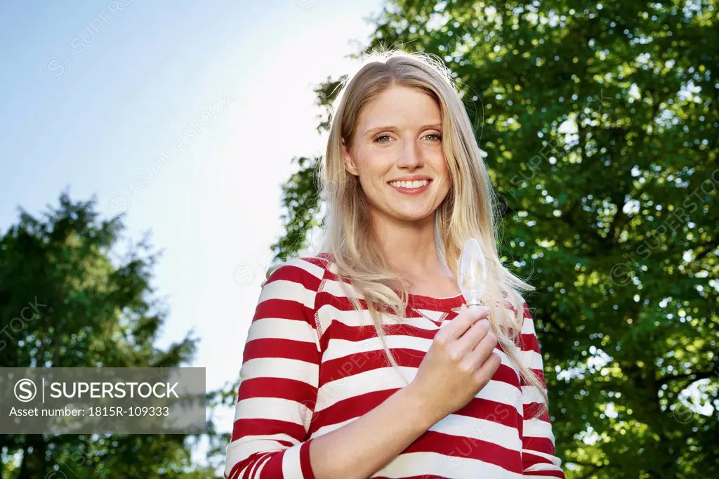 Germany, Cologne, Young woman holding lightbulb, smiling, portrait