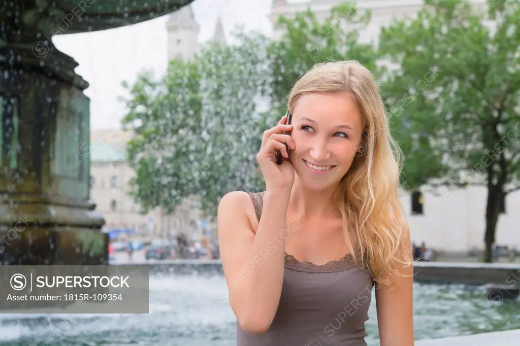 Germany, Bavaria, Munich, Young woman talking on phone in front of Ludwig Maximilian University, smiling