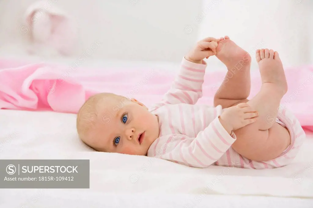 Baby girl lying on baby blanket with holding foot