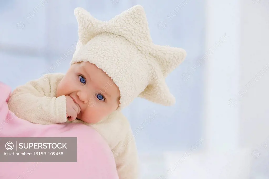 Baby girl in star shape hat with finger in mouth