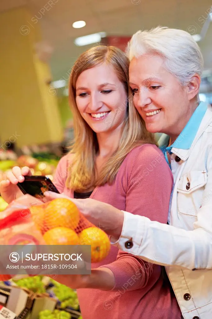 Germany, Cologne, Womens with smart phone and oranges in supermarket