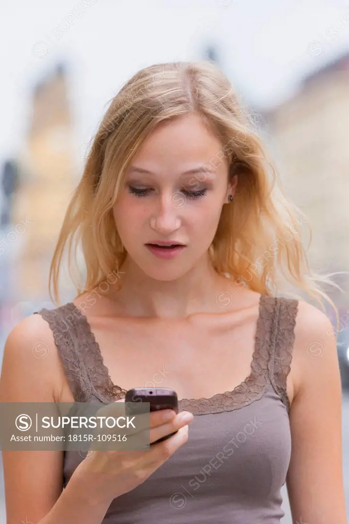 Germany, Bavaria, Munich, Young woman with smart phone in front of Bavarian State Library at Ludwigstrasse