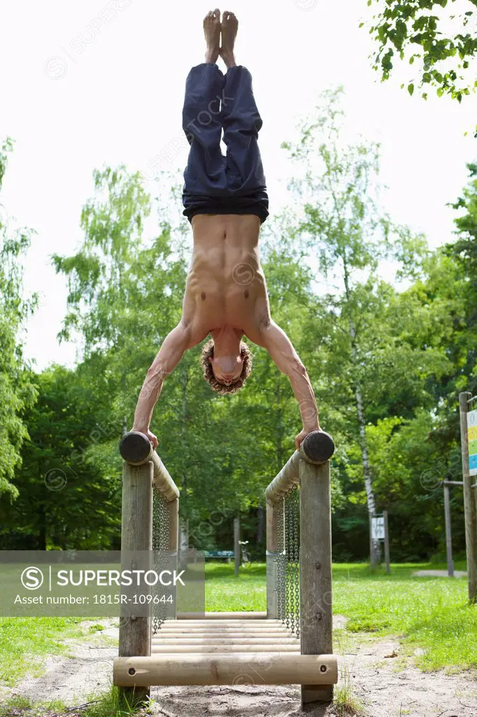 Germany, Bavaria, Young man doing handstand on railing