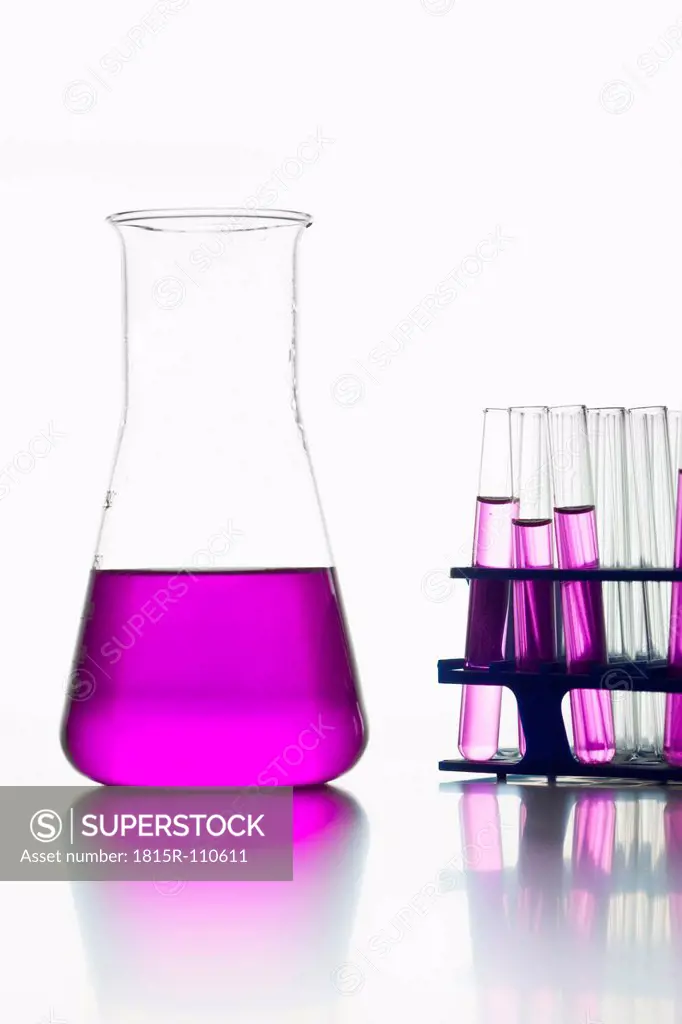 Test tubes with pink solution and volumetric flask on white background, close up