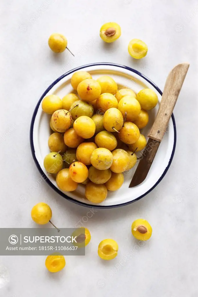 Bowl of mirabelles and a kitchen knife on white background