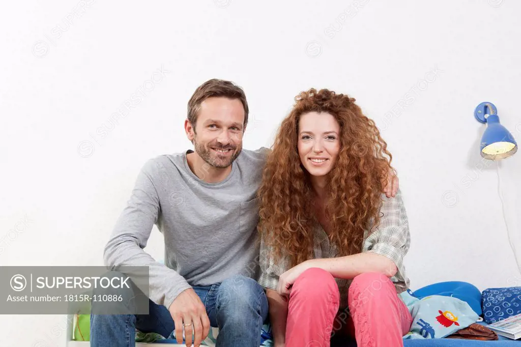 Germany, Berlin, Couple sitting on bed, smiling, portrait