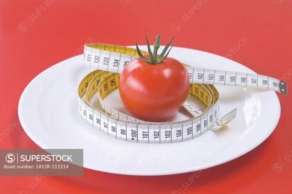 Red tomato on plate with measuring tape, close up