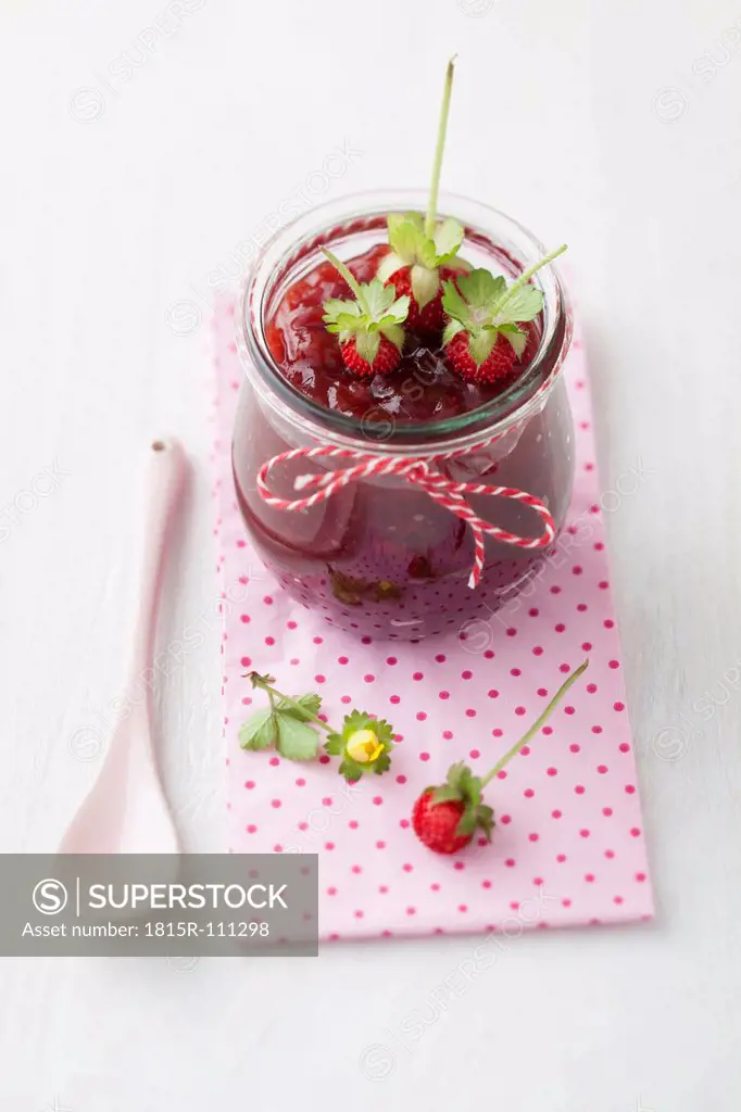 Jar of wild strawberry jam with spoon on white background