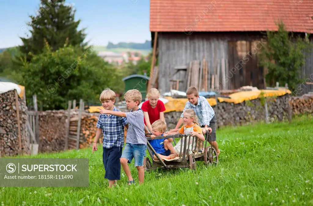 Germany, Bavaria, Group of children playing with hand cart in front of farmhouse