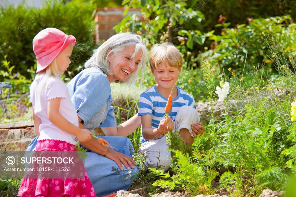 Germany, Bavaria, Grandmother with children inspecting carrots in garden