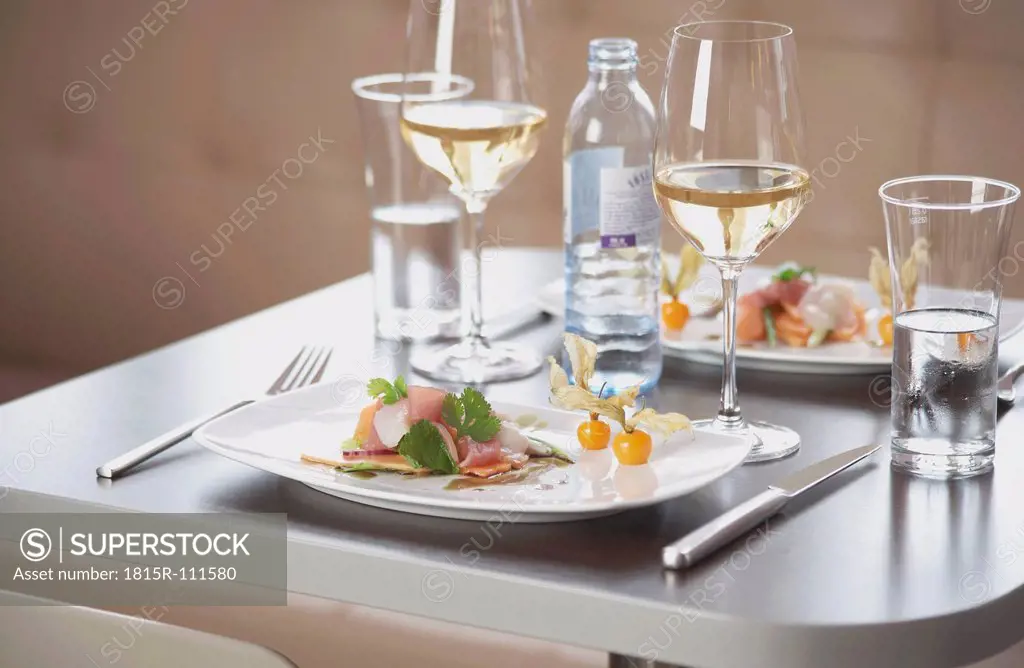 Plate of ham and cantaloupe with wine glass on table