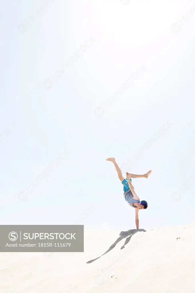 France, Teenage boy making handstand on sand dune