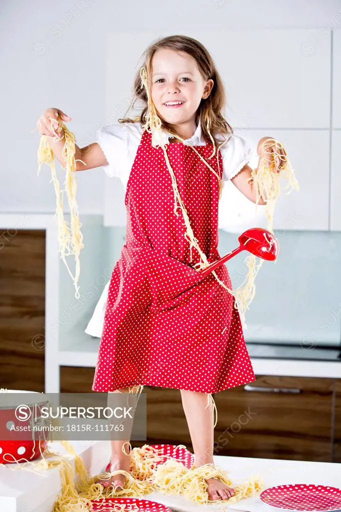 Germany, Girl playing with spaghetti on kitchen worktop