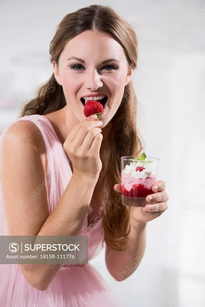 Germany, Young woman biting strawberry, close up