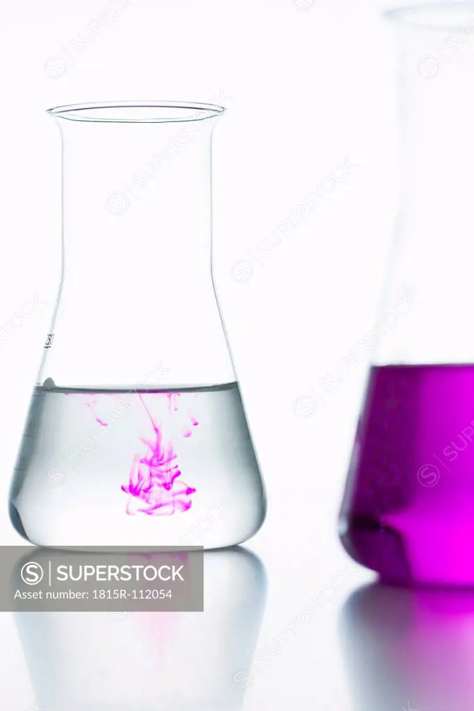 Volumetric flasks with colorless and pink on white background, close up