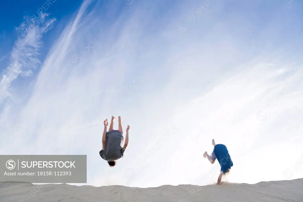 France, Two boys jumping on sand dune