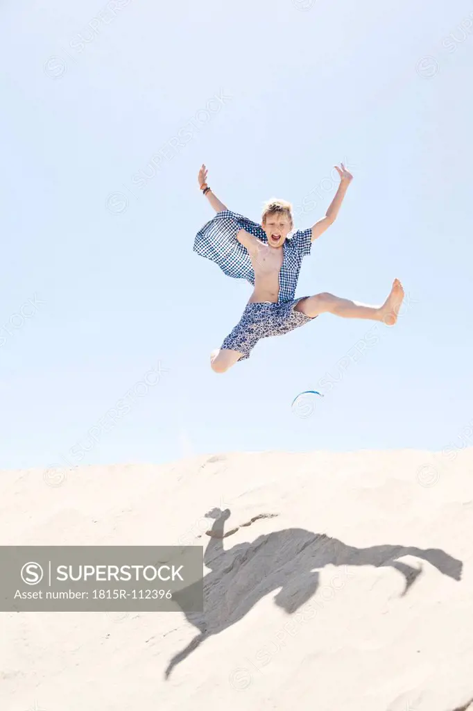 France, Boy jumping on sand dune