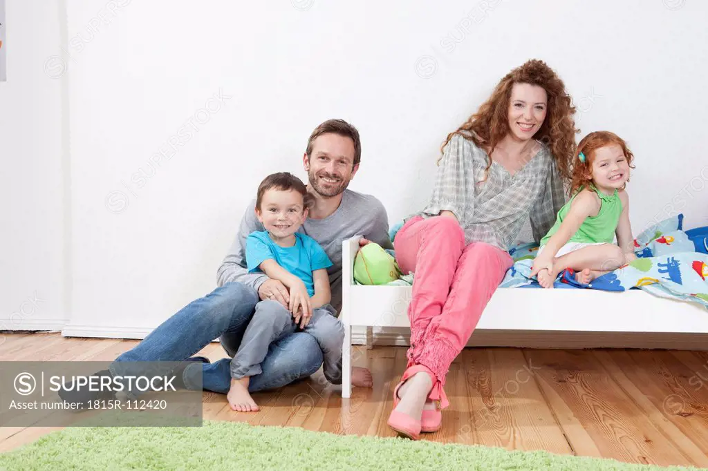 Germany, Berlin, Family sitting on bed, smiling, portrait