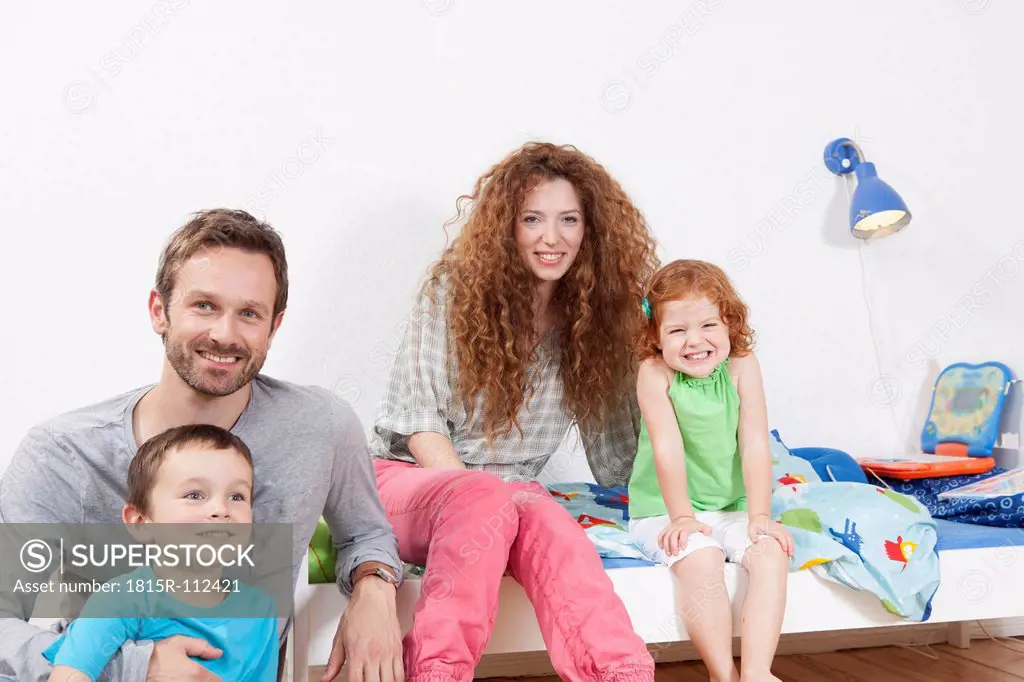 Germany, Berlin, Family sitting on bed, smiling, portrait