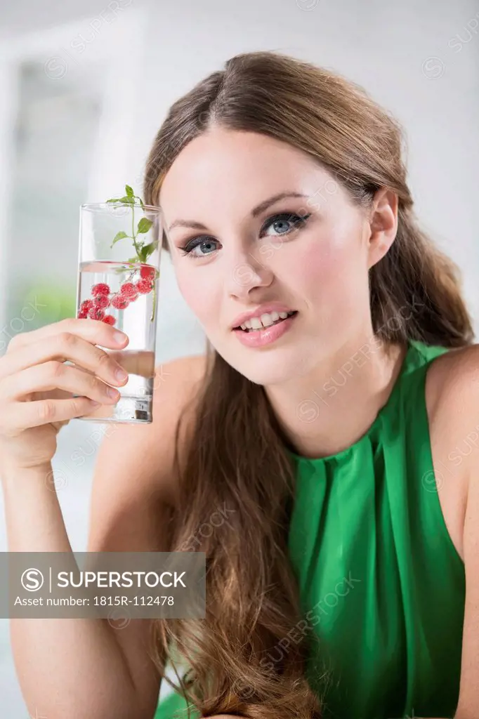 Germany, Young woman holding glass of water with berries