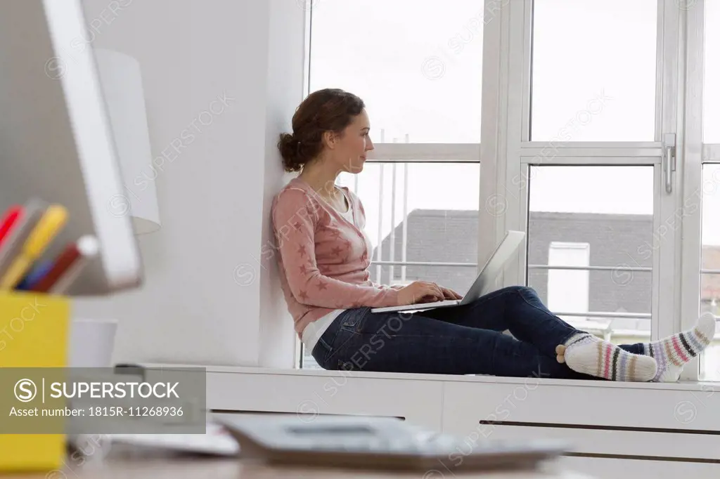 Woman sitting on windowsill using laptop